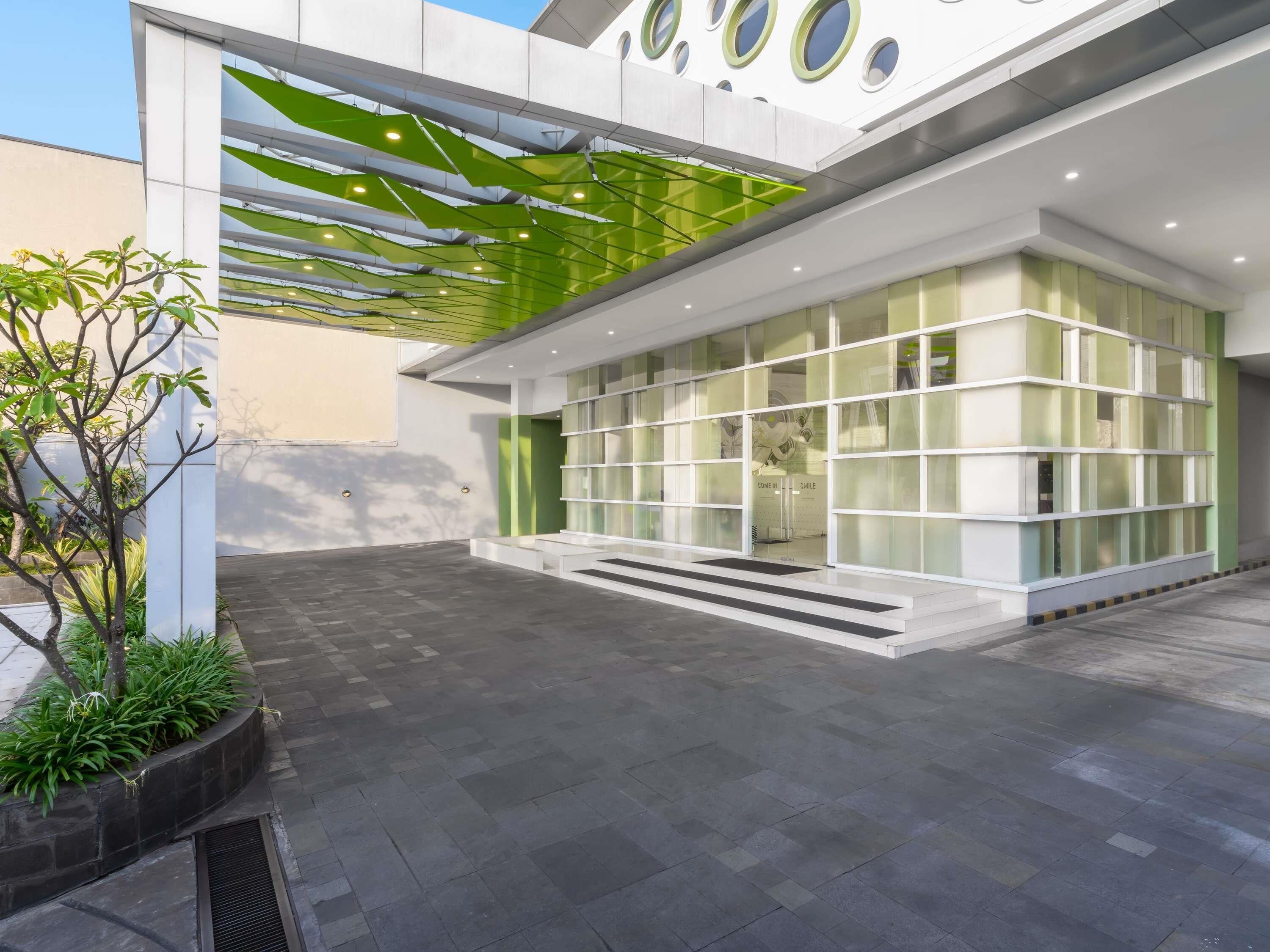 Un edificio moderno con fachada de vidrio, techo verde y un área de entrada pavimentada.