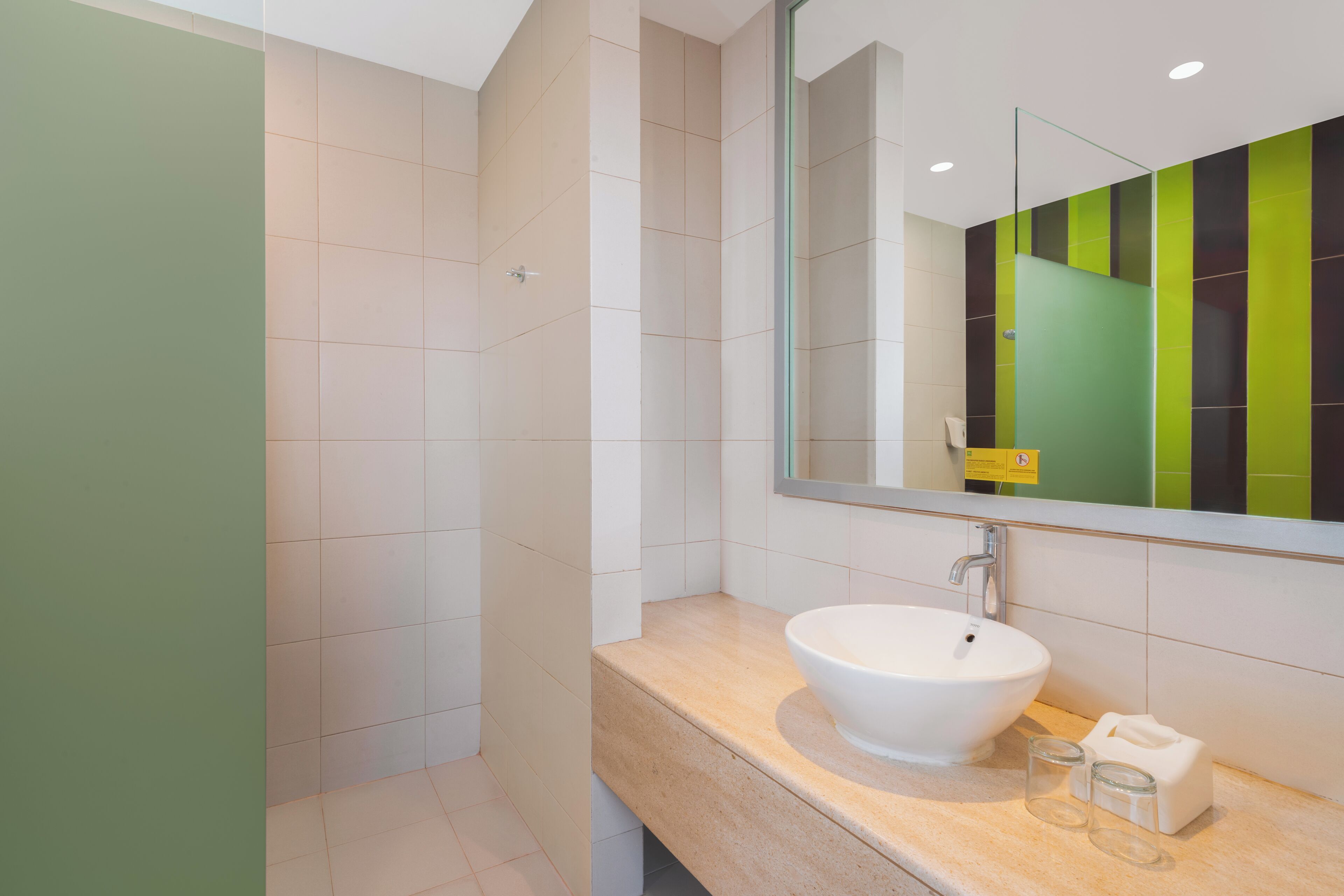 A modern bathroom with a white sink, a large mirror, and a green and black tiled wall.