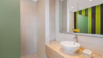 A modern bathroom with a white sink, a large mirror, and a green and black tiled wall.