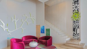 A modern lobby with a staircase, red velvet sofas, a white coffee table, and abstract wall art. - Ibis Styles Malang (Malang)