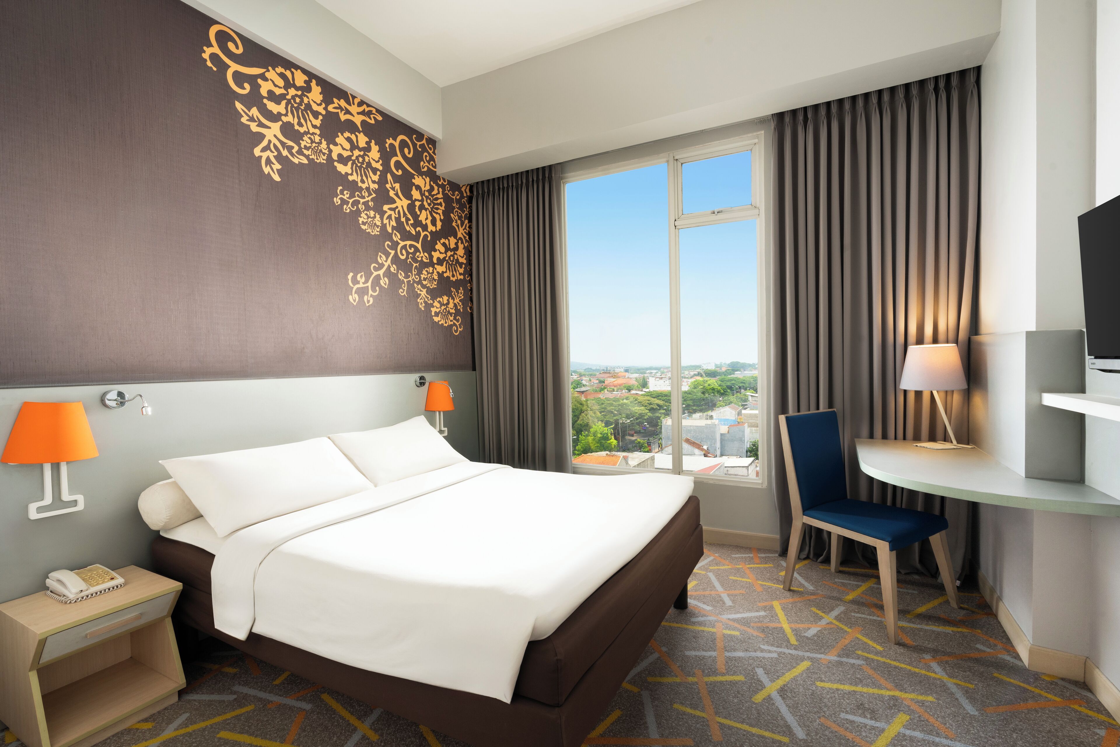 A hotel room with a large bed, two bedside lamps, a desk with a chair, and a TV.
