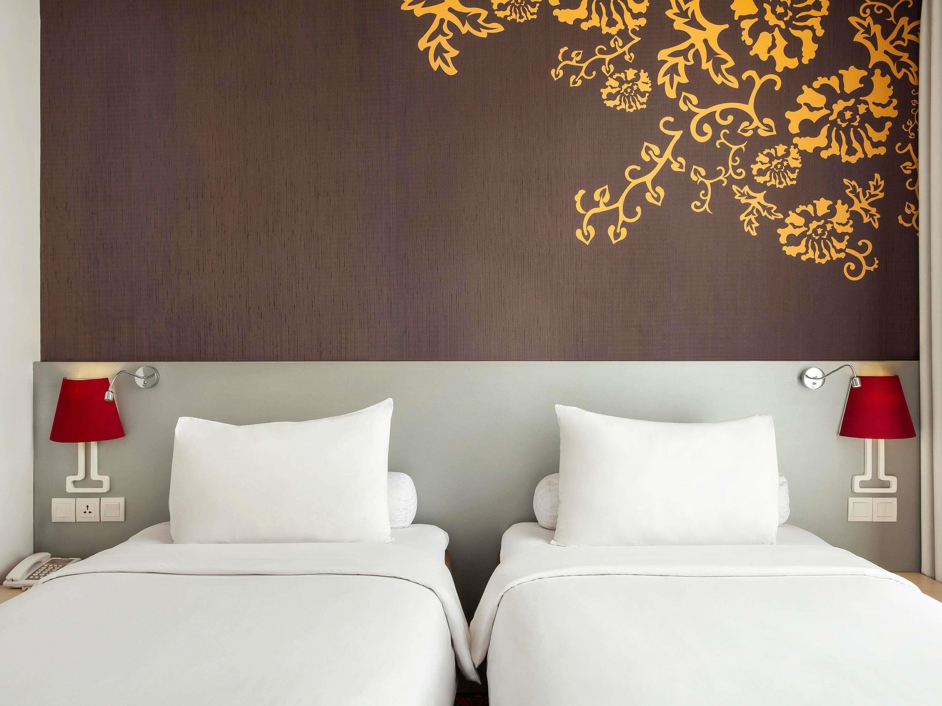 A hotel room with two beds, a wooden headboard, and red lamps.