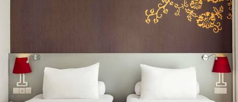 A hotel room with two beds, a wooden headboard, and red lamps.