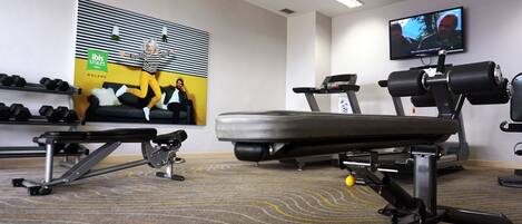 A gym with exercise equipment, a television, and a wall-mounted poster.