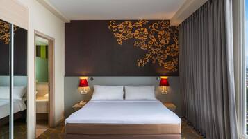 A hotel room with a large bed, two bedside lamps, a wall with floral patterns, a window with curtains, and a patterned carpet.
