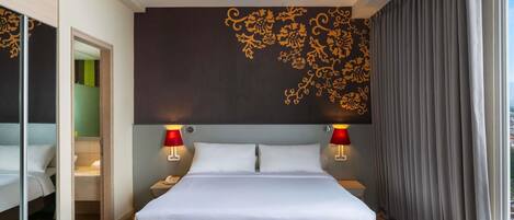 Habitación de hotel con una cama grande, dos lámparas de noche, una pared con motivos florales, un ventanal con cortinas y una alfombra estampada.