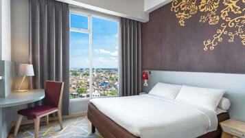 Habitación de hotel con una cama grande, un escritorio con silla, una mesita de noche y vistas a la ciudad a través de un ventanal amplio.