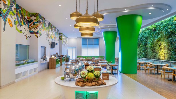 A modern restaurant with a central serving area, green vertical garden wall, and colorful mural. - Ibis Styles Malang (Malang)