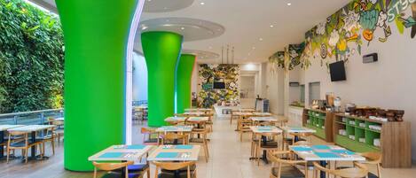 A modern restaurant with green pillars, wooden tables, and a colorful mural on the wall.