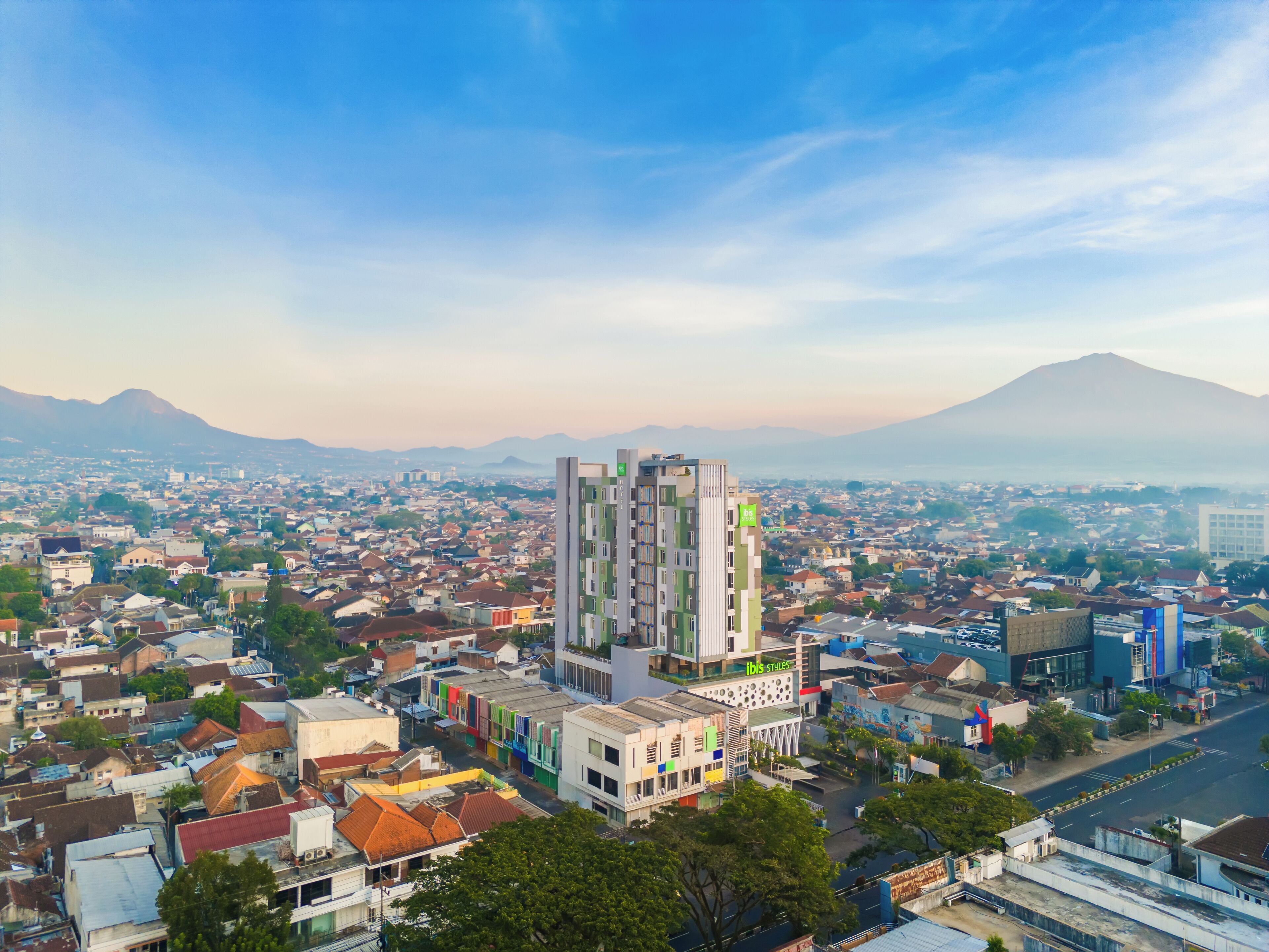 Un paisaje urbano con un rascacielos destacado en el centro, rodeado de edificios más bajos y una montaña al fondo.
