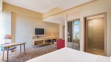 A hotel room with a bed, a desk, a television, a shower, and a view of the city.