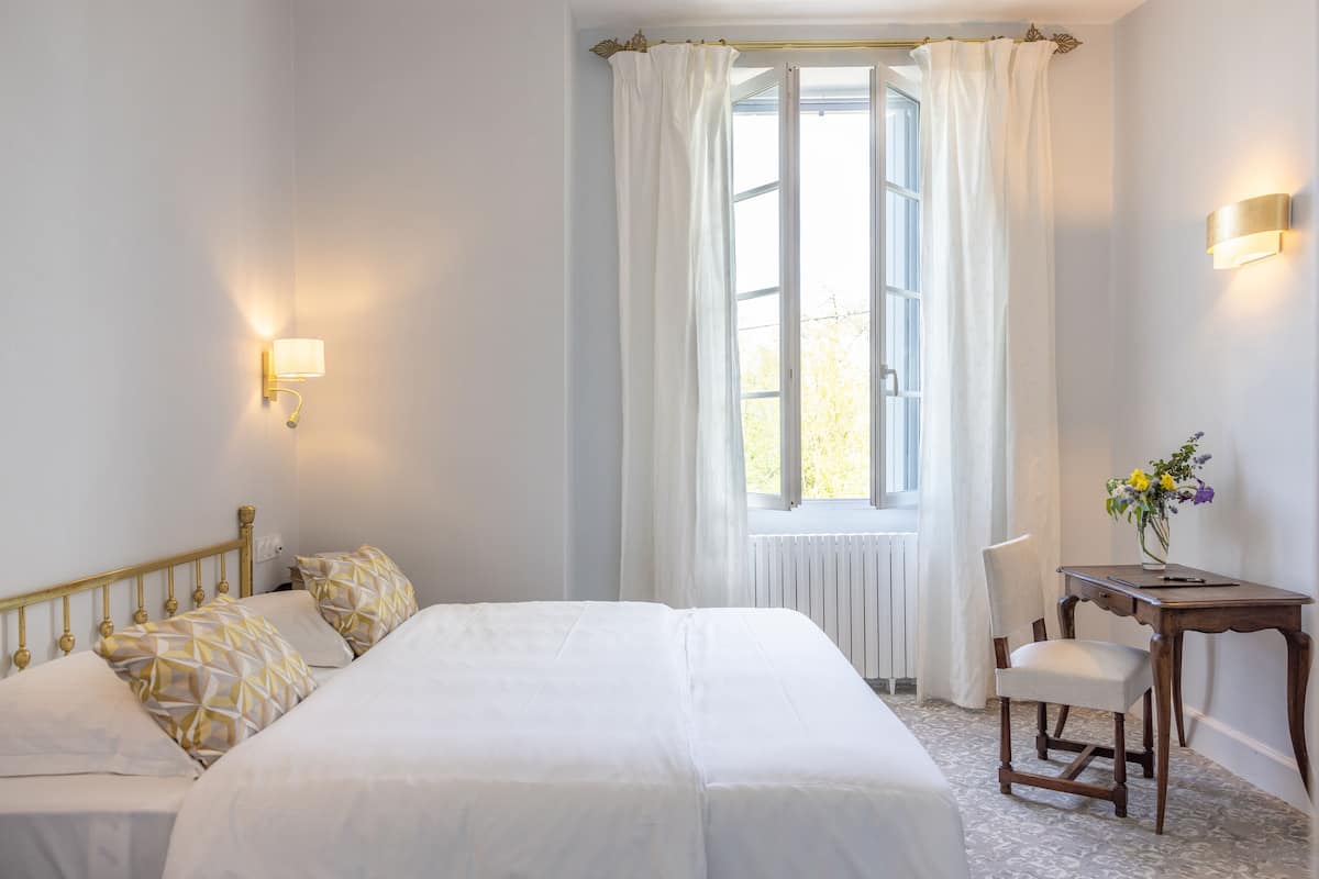 A hotel room with a large bed, two bedside tables, a chair, and a window with curtains.