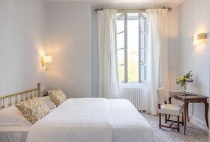 Une chambre d’hôtel avec un grand lit, deux tables de chevet, une chaise et une fenêtre avec des rideaux.