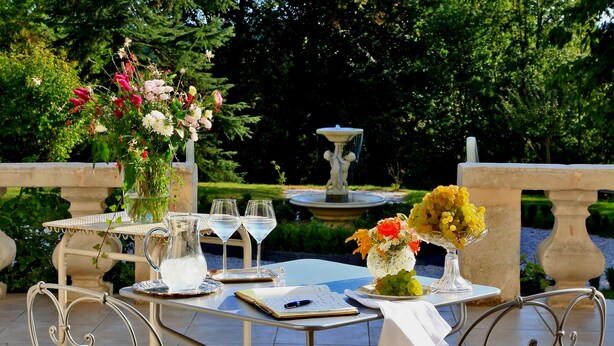 An outdoor dining area with two metal chairs, a table with a white tablecloth, and a vase of flowers. - Château Bellevue (Cazaubon)