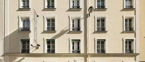 Um edifício com a placa "MISTRAL HOTEL" sobre a entrada. Possui várias janelas com sacadas, e o edifício apresenta um estilo arquitetônico clássico.