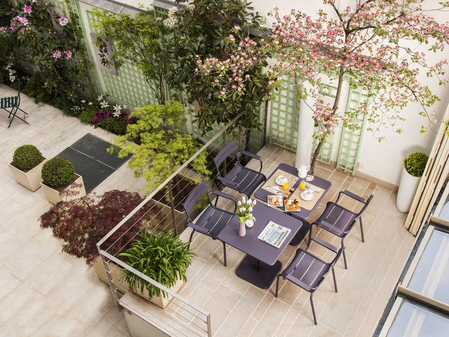 An outdoor patio with a table set for dining, surrounded by chairs, and a variety of plants and flowers.