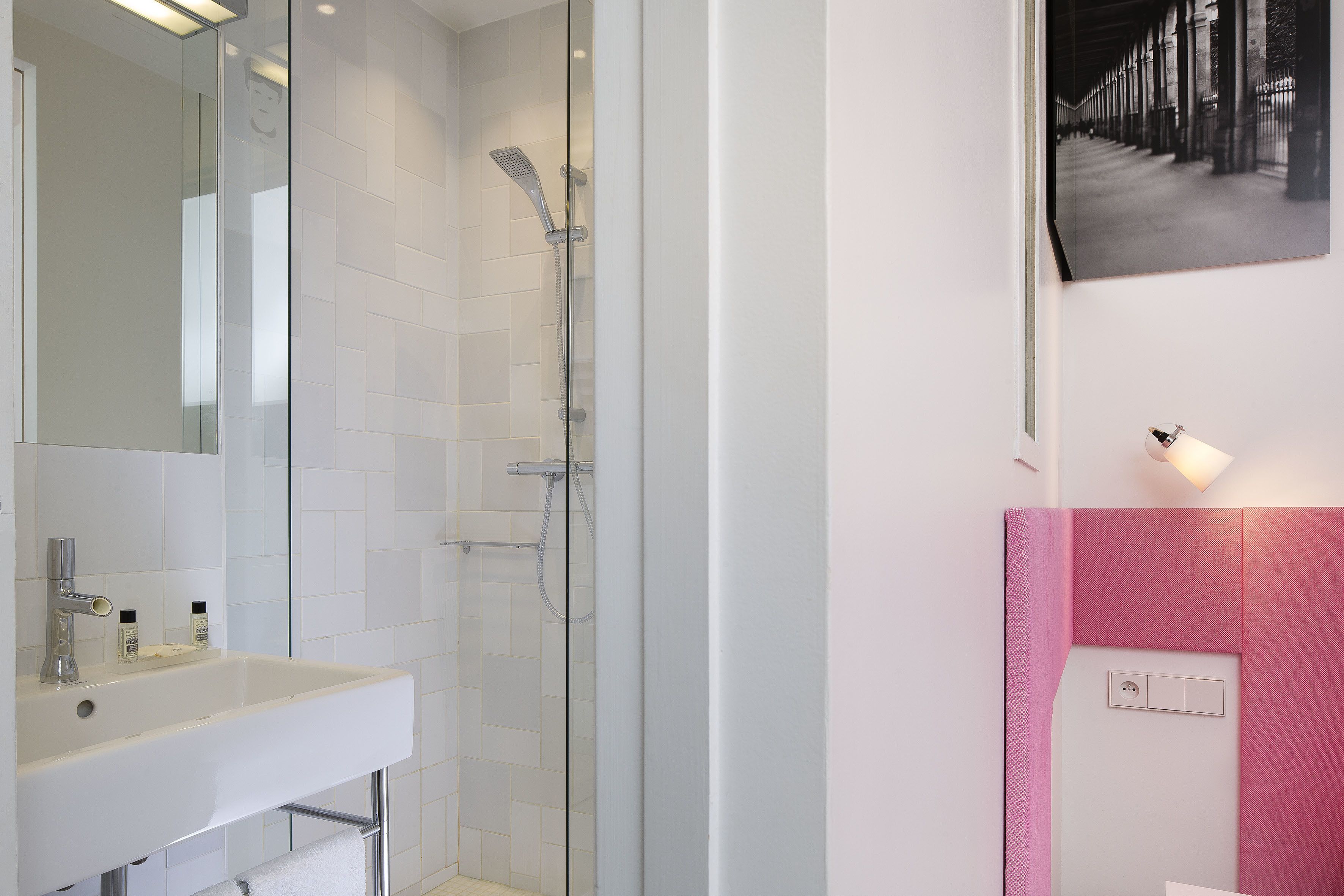 A modern bathroom with a glass-enclosed shower, a white sink with a mirror, and a pink accent wall.