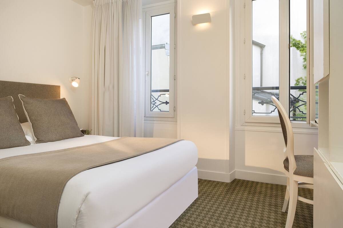 Una habitación de hotel con cama, una silla, ventana y balcón.