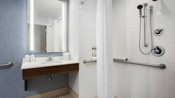 A bathroom with a white sink, mirror, and shower with grab bars.