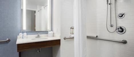 A bathroom with a white sink, mirror, and shower with grab bars.