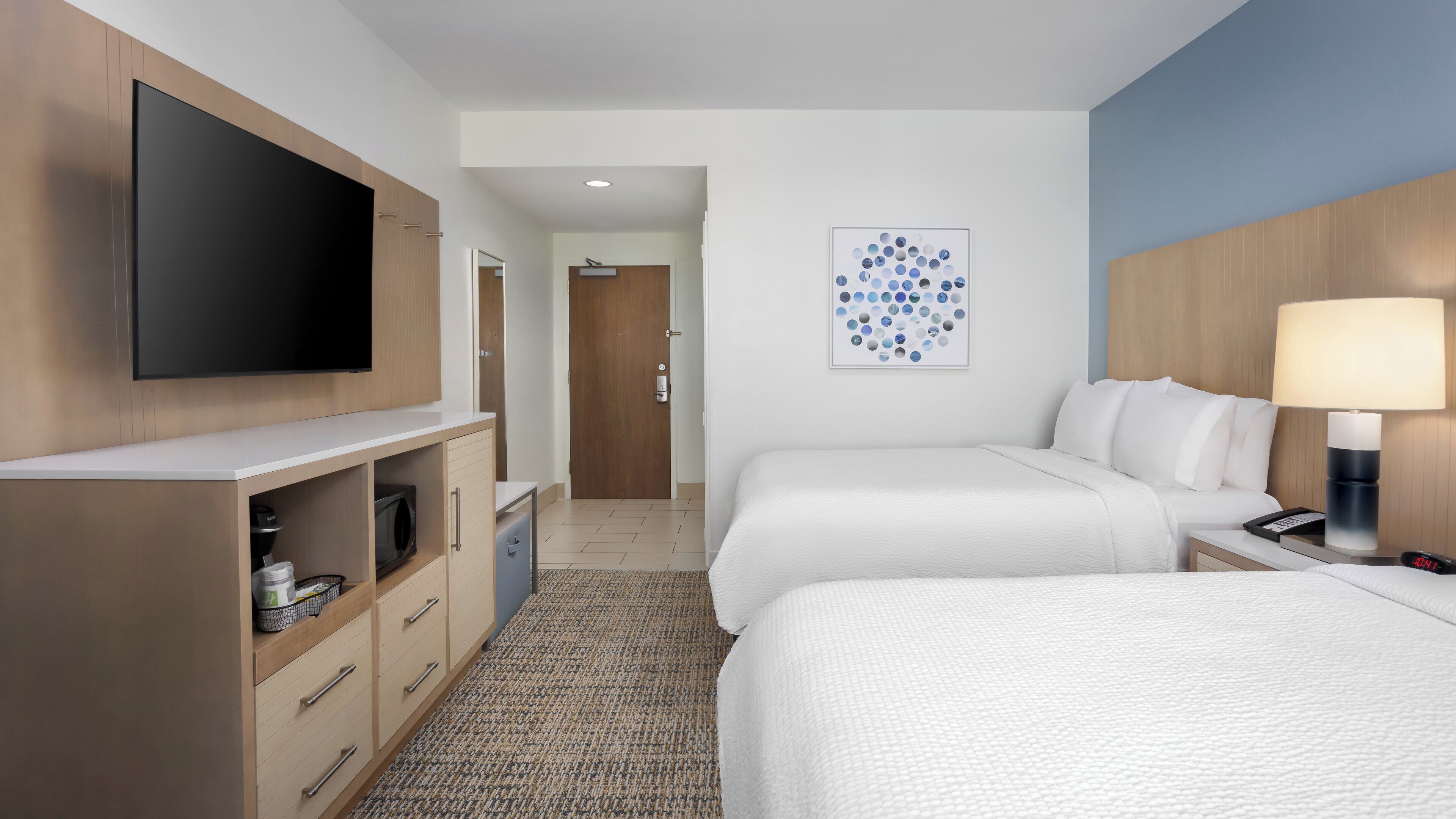 A hotel room with two beds, a TV, a desk, a lamp, and a wall art piece.