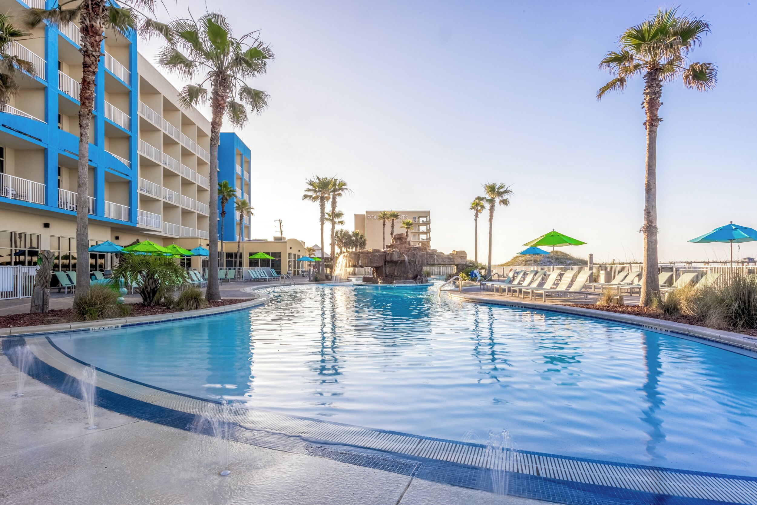 A swimming pool with palm trees, lounge chairs, and a hotel building in the background.