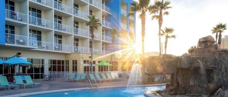 A hotel with a swimming pool, palm trees, and a waterfall feature.