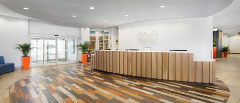 Un área de recepción con un mostrador de madera, piso estampado y plantas en macetas.