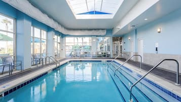 An indoor swimming pool with clear blue water, metal pool ladders, and a skylight above.