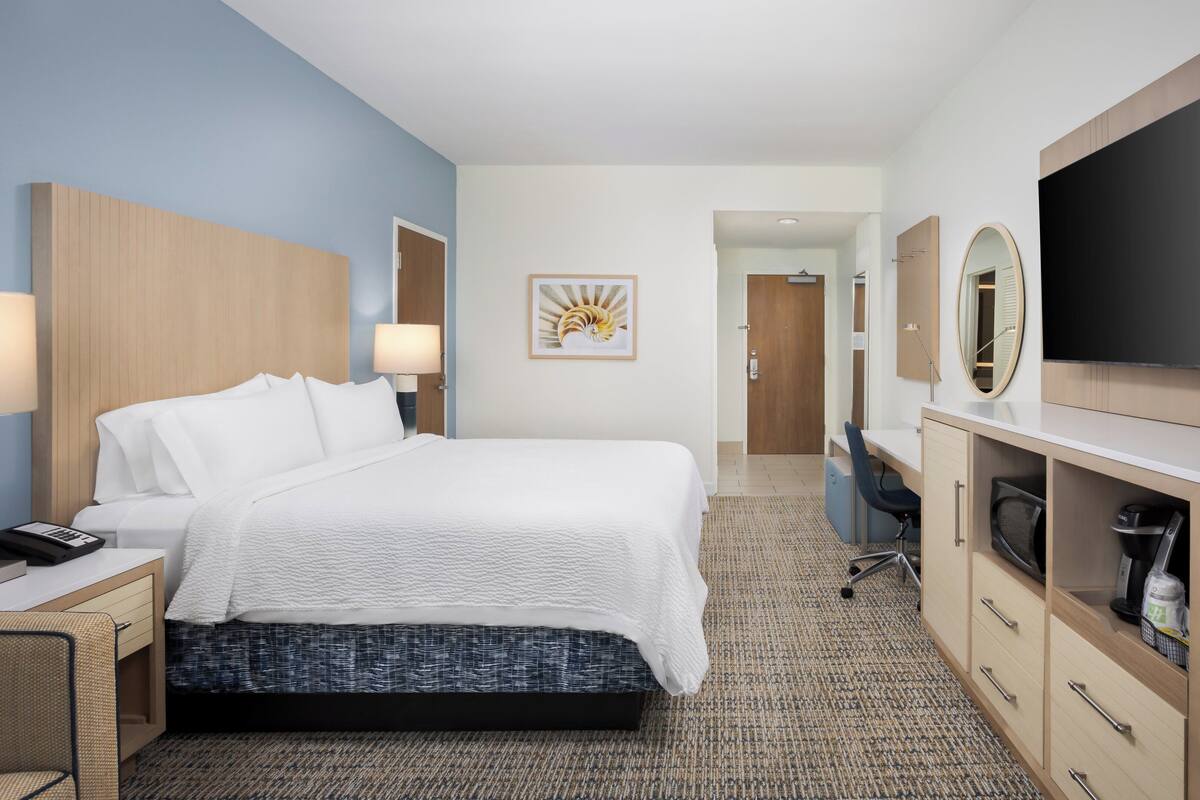 A hotel room with a bed, desk, TV, and a painting on the wall.