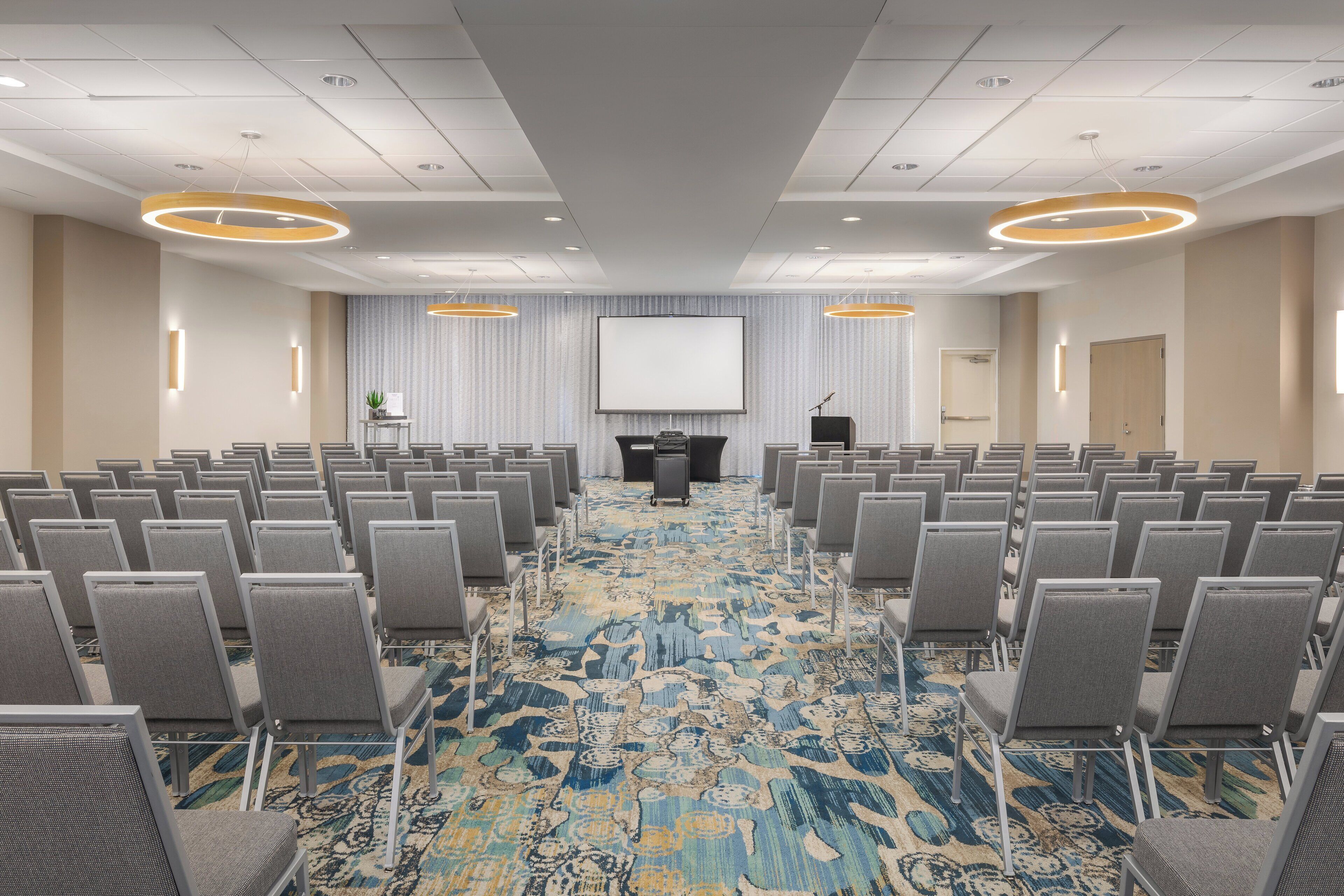 A conference room with rows of chairs, a large screen, and a podium.