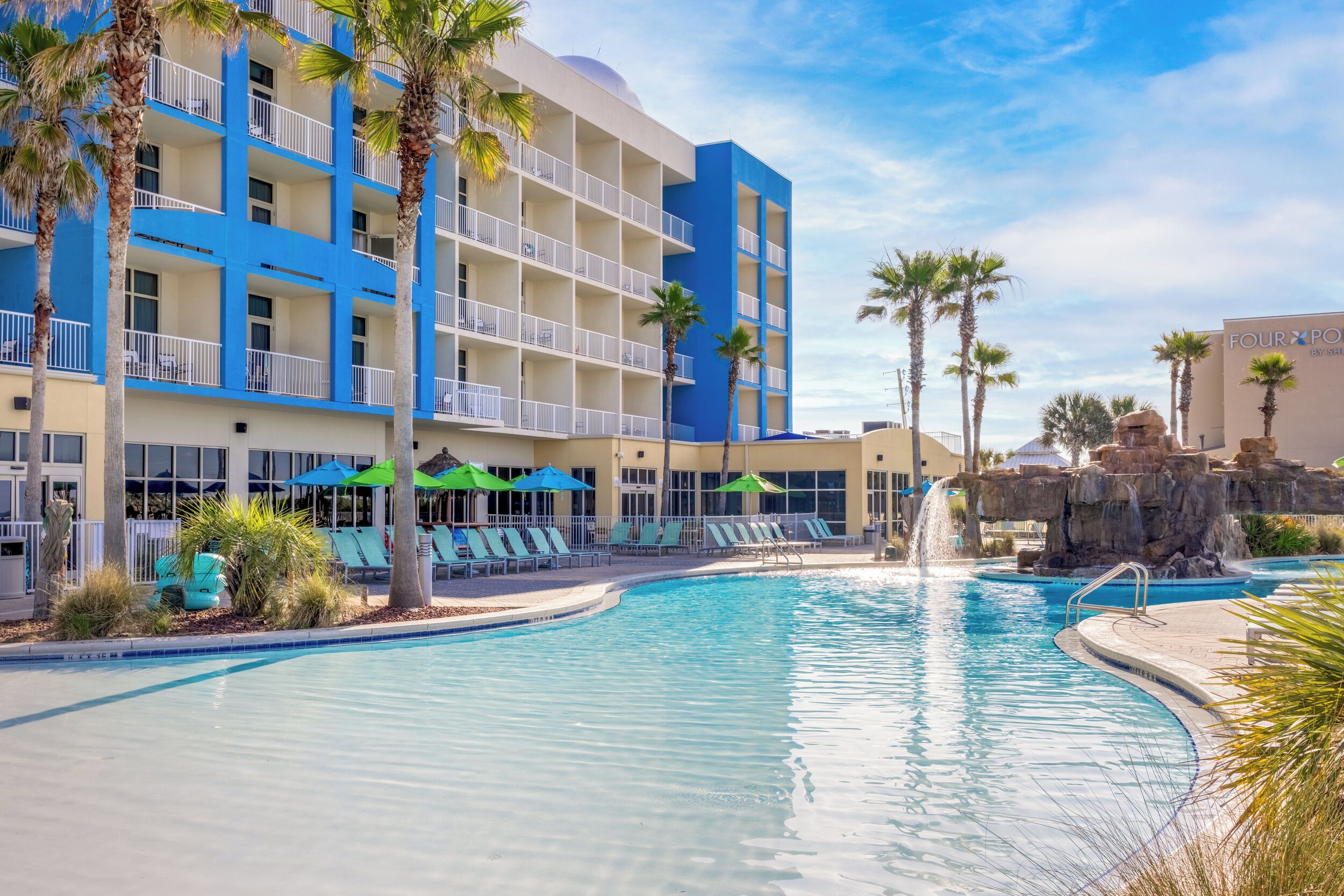 A hotel with a swimming pool, palm trees, and a waterfall feature.