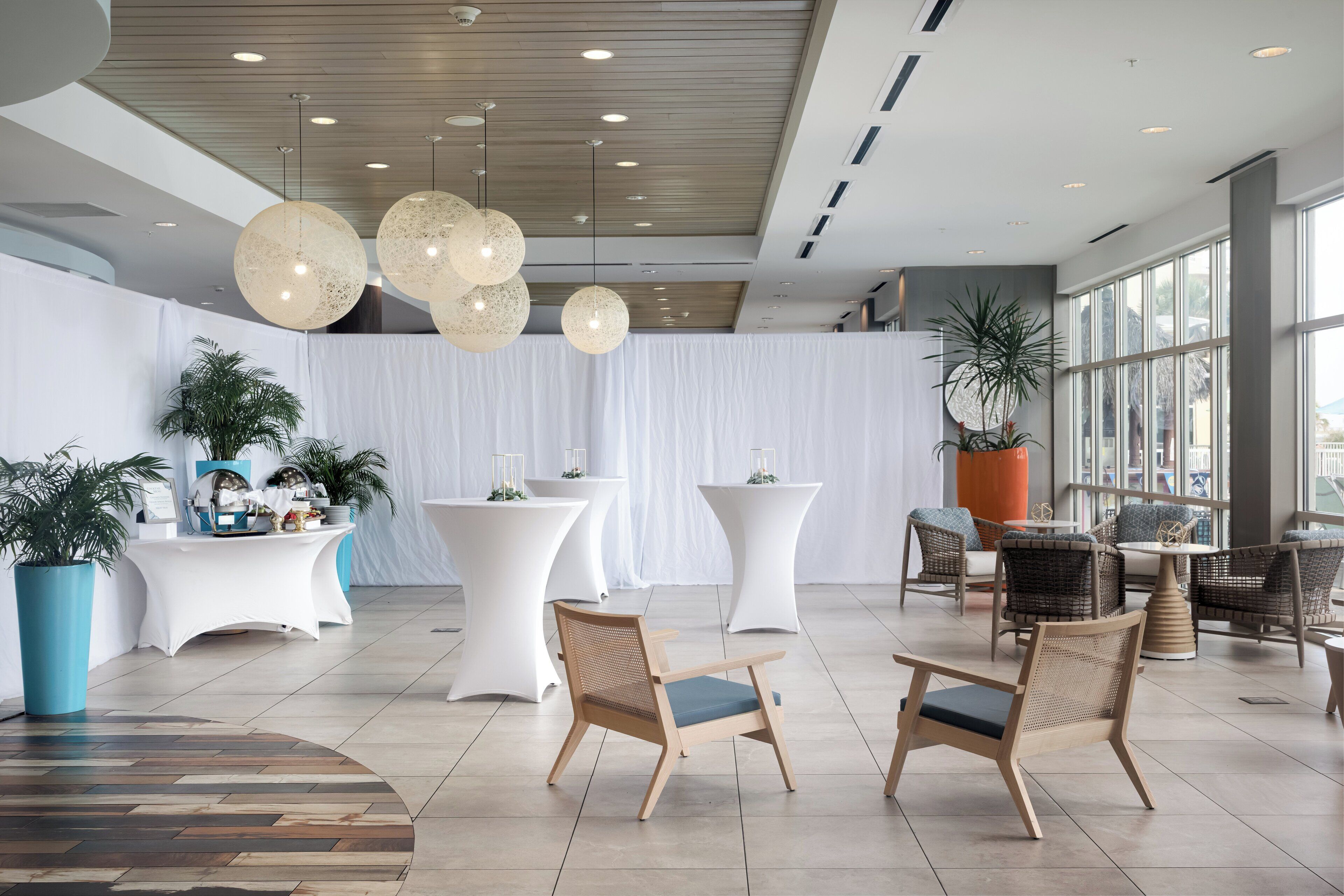 Un espacio interior moderno con mesas redondas, sillas de mimbre e iluminación esférica colgante.