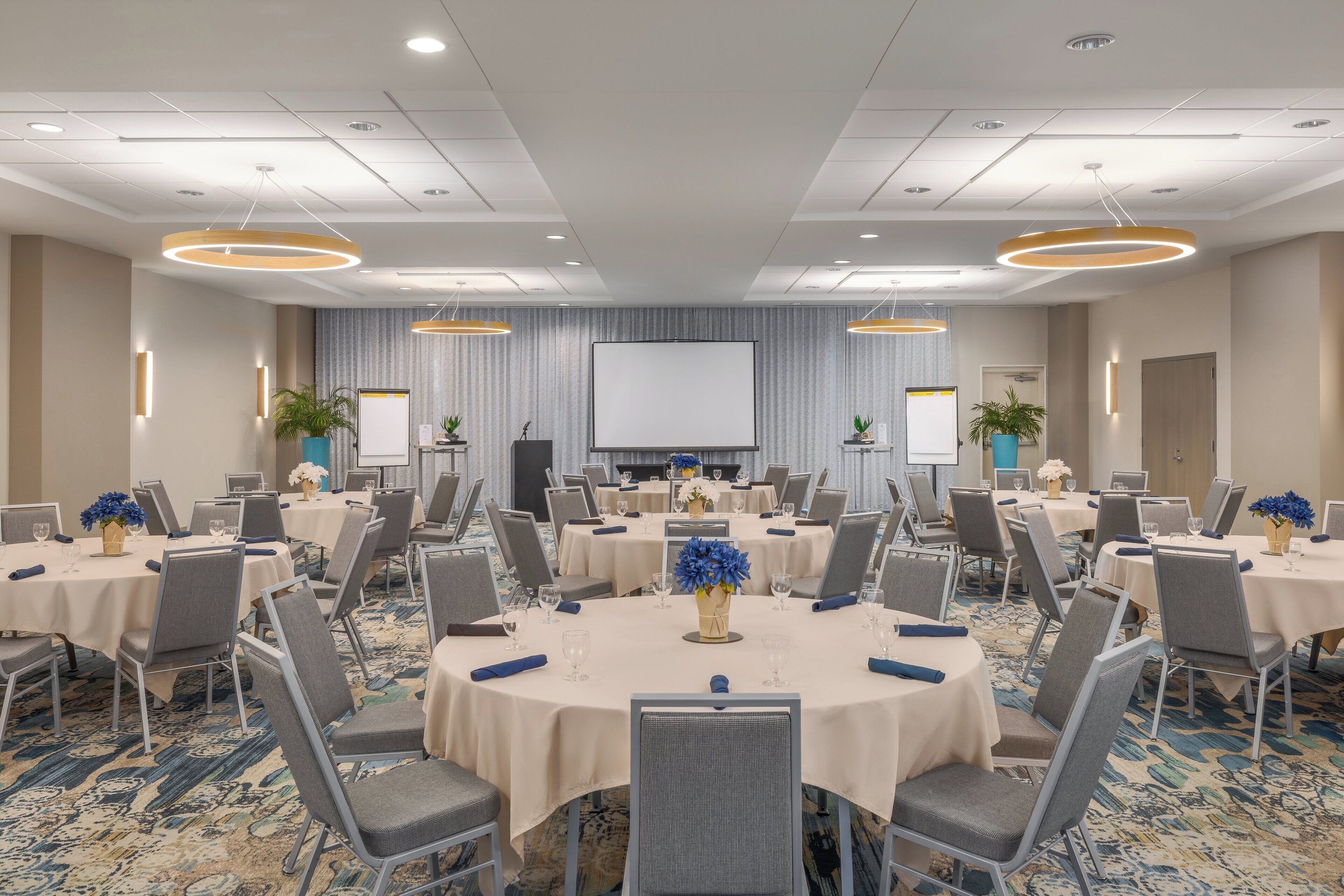 A conference room with round tables, chairs, and a large screen at the front.