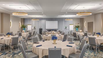 A conference room with round tables, chairs, and a large screen at the front.