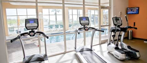 A gym with treadmills and an exercise bike, large windows, and a view of a pool area.