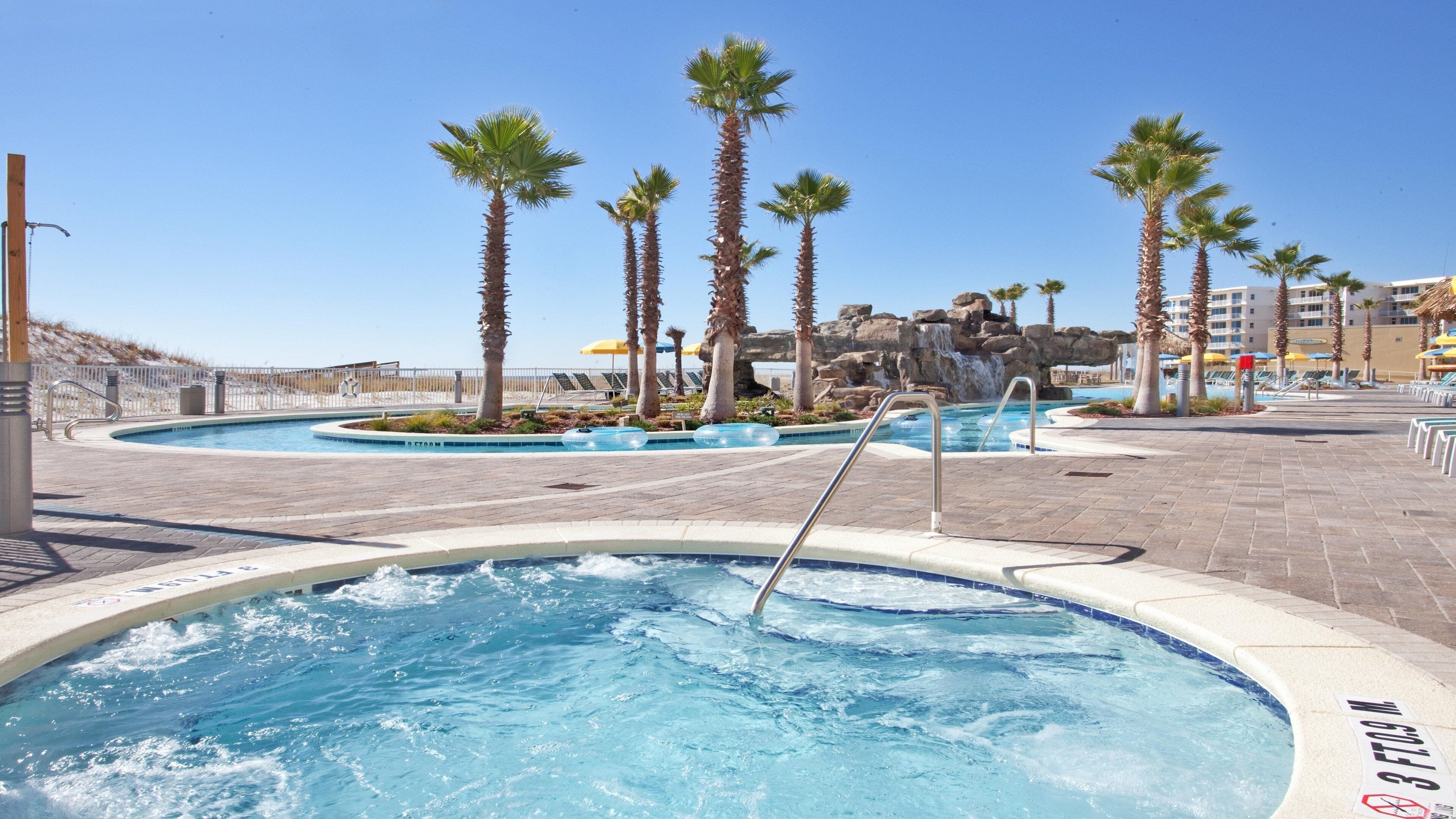 A pool area with hot tubs, palm trees, and a waterfall feature.