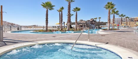 Un área de piscina con jacuzzis, palmeras y una cascada.