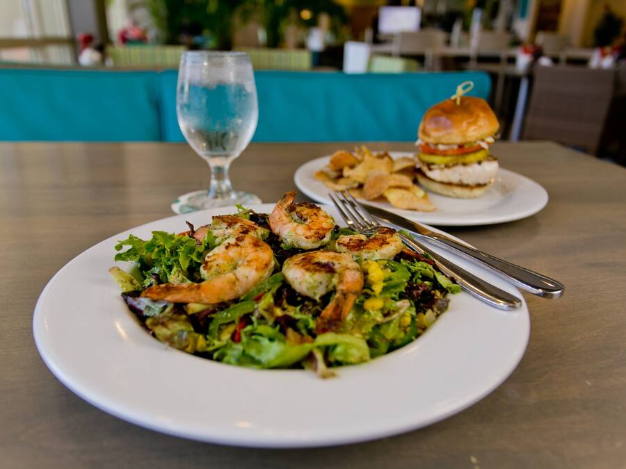 A dining table with a plate of shrimp salad and a burger.