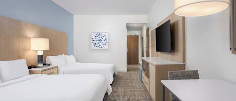 A hotel room with two beds, a desk, a TV, and a lamp.
