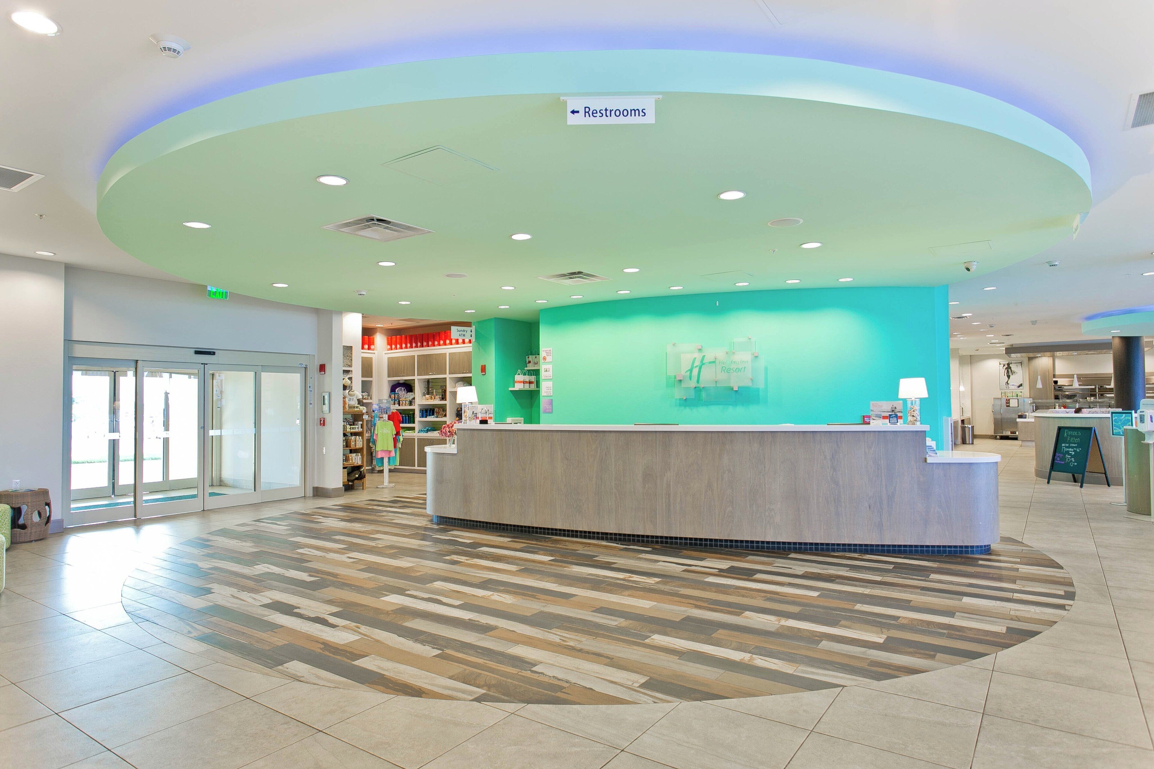 A hotel reception area with a curved counter, a sign for restrooms, and a view of the lobby.