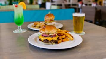 Un ambiente de restaurante con una hamburguesa y papas fritas sobre una mesa, una bebida verde y una jarra de cerveza.