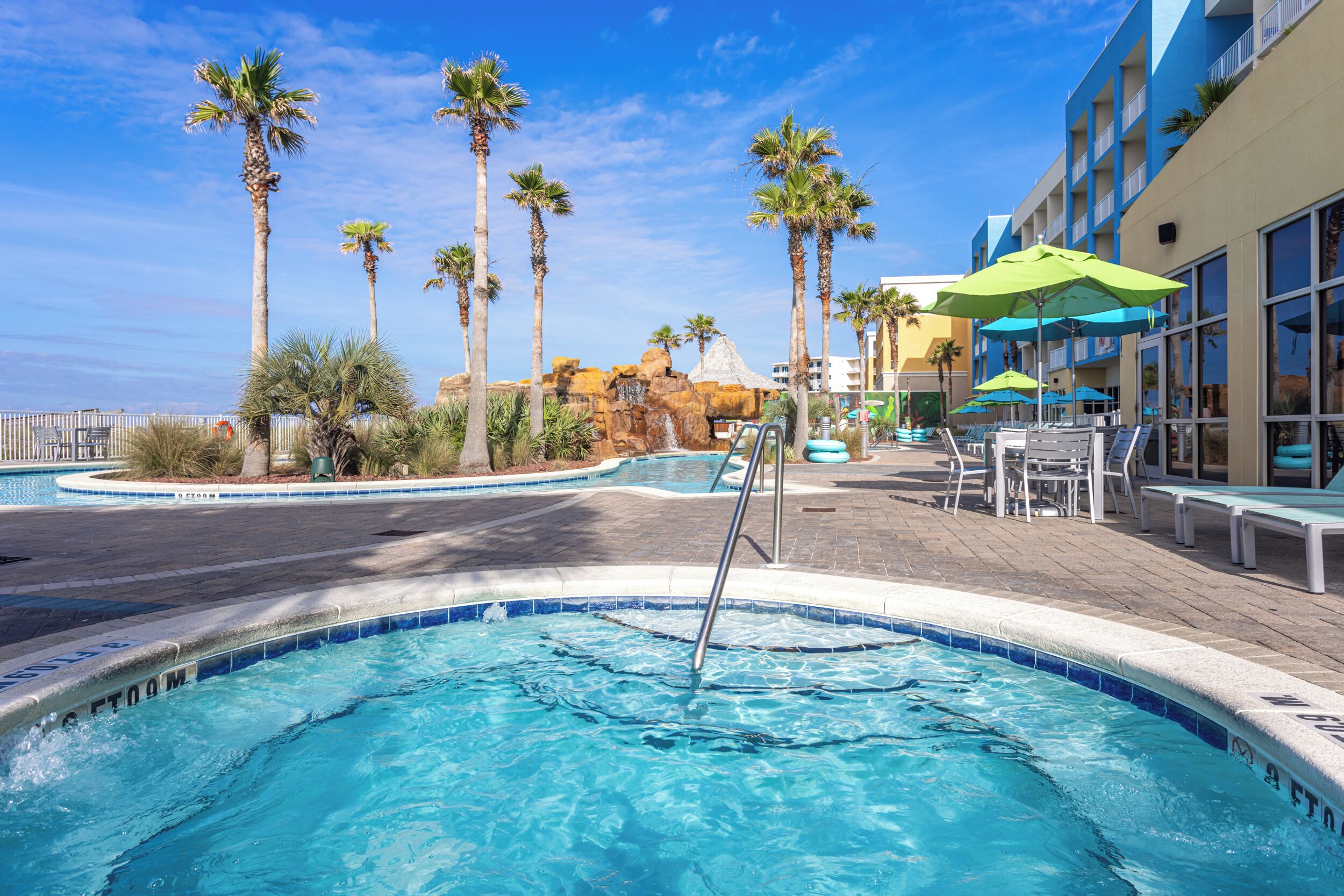 A swimming pool area with palm trees, lounge chairs, and a building with large windows.