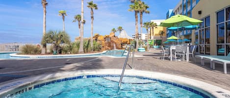 A swimming pool area with palm trees, lounge chairs, and a building with large windows.