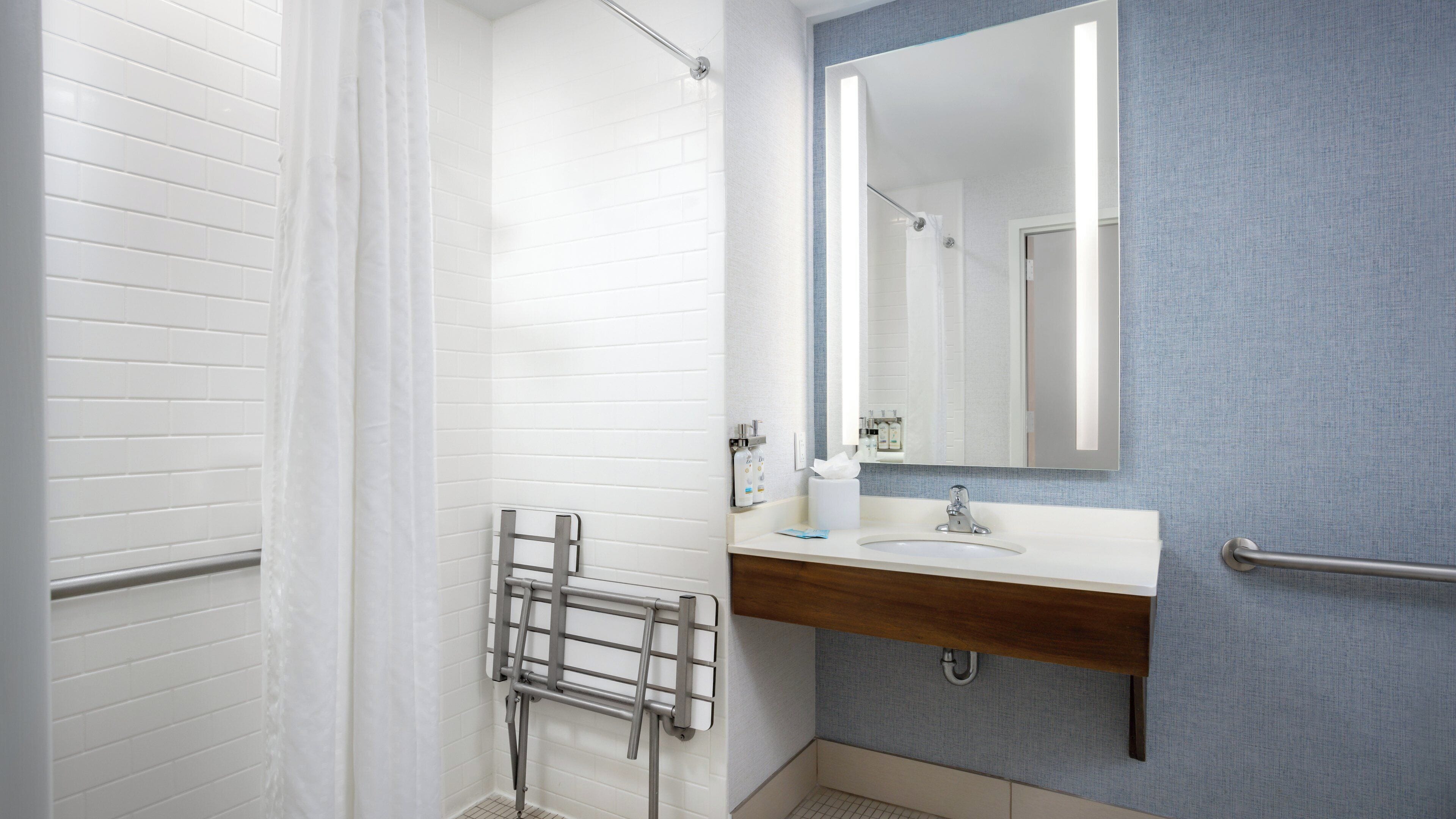 A bathroom with a white tiled shower, a wooden vanity with a mirror, and a towel rack.