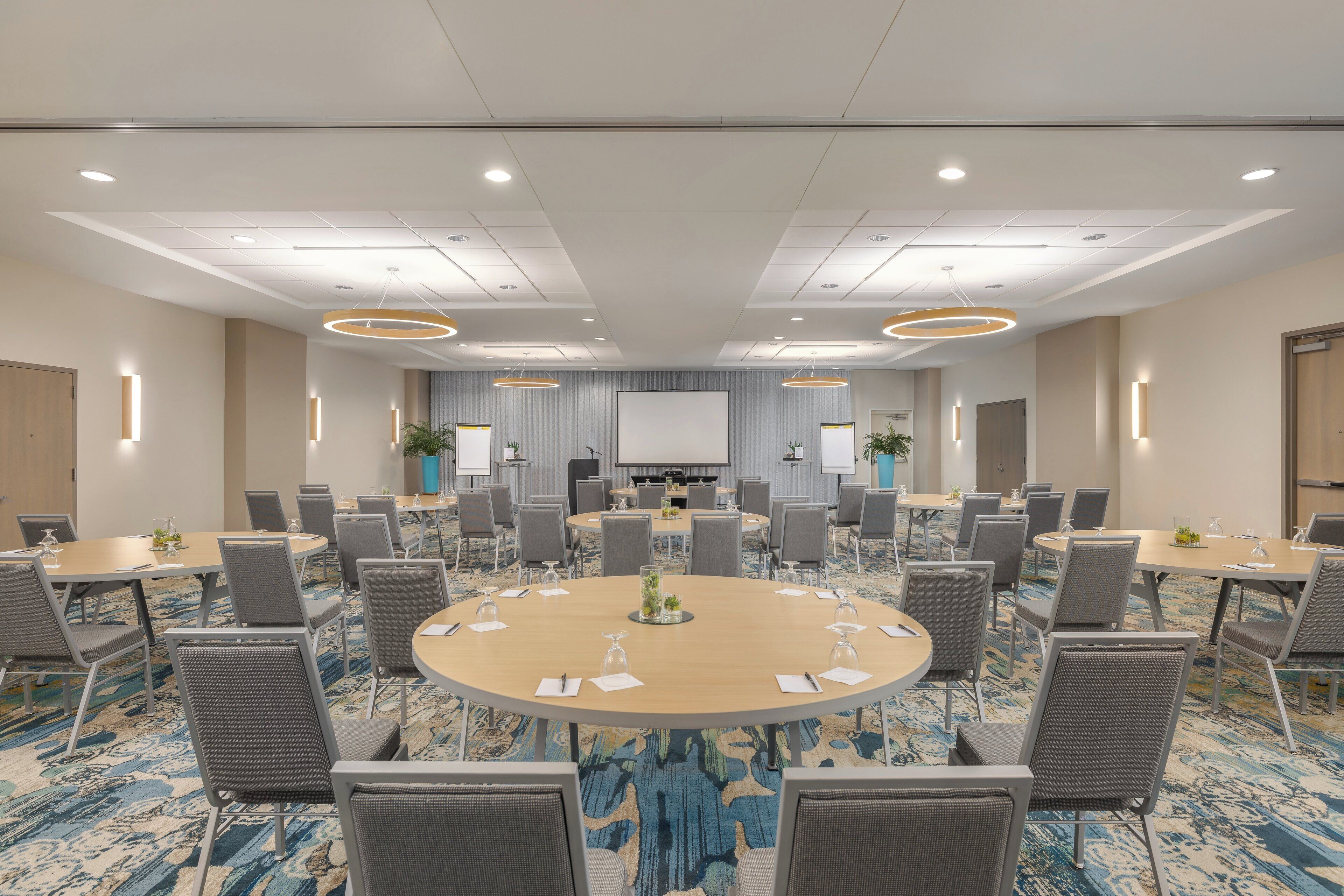 Une salle de conférence équipée d’une grande table ronde, de nombreuses chaises et d’un écran de projection.