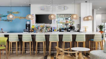 Zona de bar con un tablero de menú, taburetes y un área de asientos con una mesa redonda.
