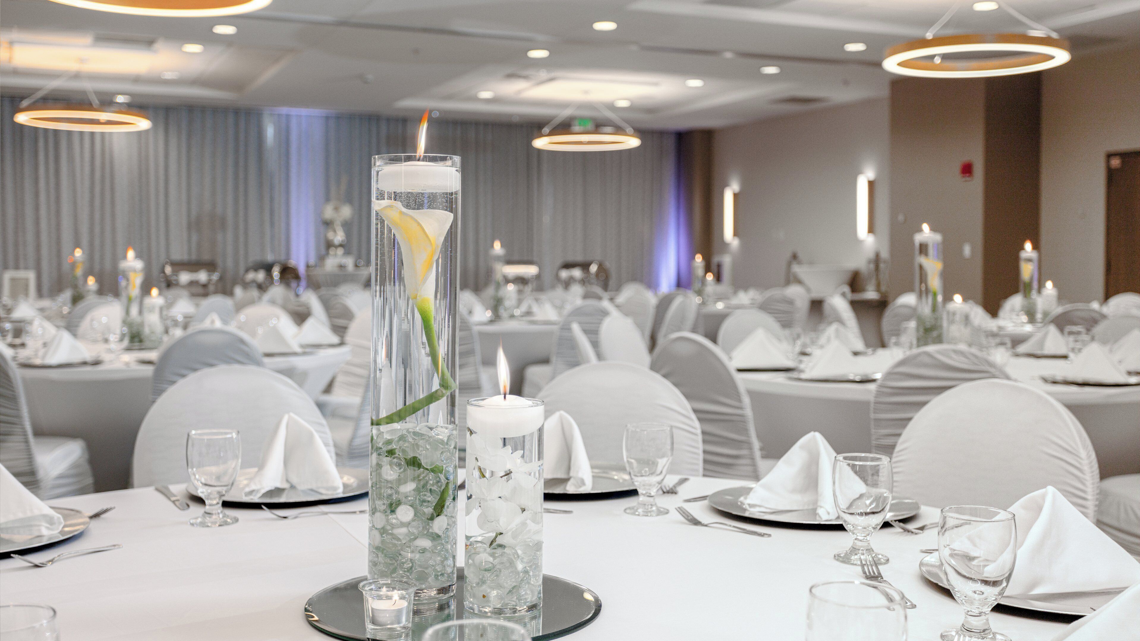 Un salón de banquetes con mesas redondas dispuestas para comer, con cubertería de vidrio transparente y manteles blancos.