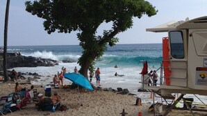 A beach scene with a lifeguard tower, beach chairs, and umbrellas. - Kona Hawaii Guesthouse (Kailua-Kona)