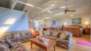 A spacious living room with high ceilings, a kitchen in the background, and a large bed with a wooden headboard. - Kona Hawaii Guesthouse (Kailua-Kona)